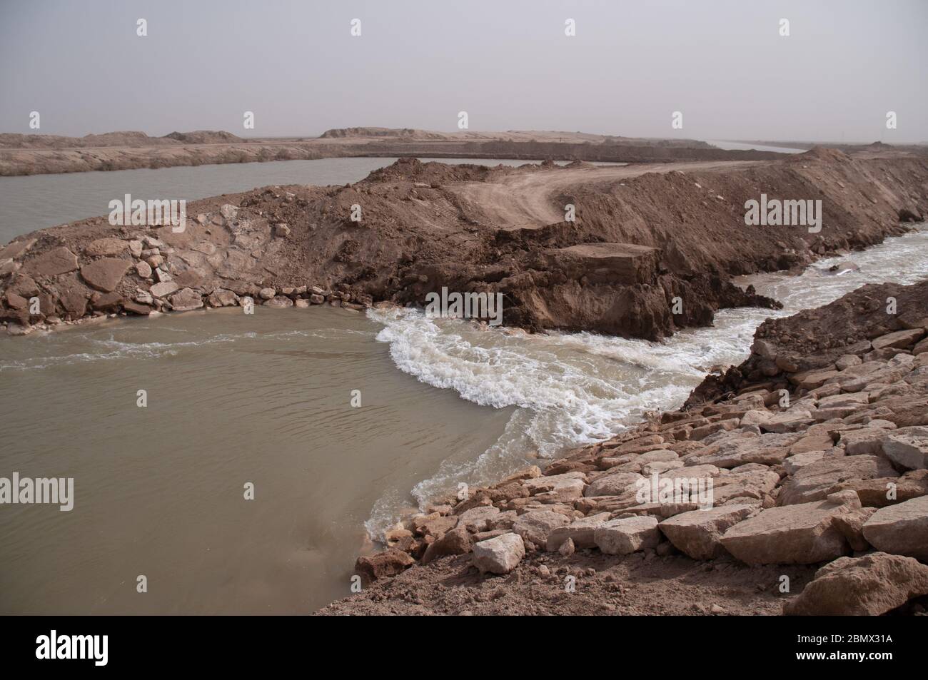 water rushes through a breached dam in Southern Iraq,  the dam was constructed by Saddam Hussein to prevent water from flowing across the marshes in southern Iraq after the end of Gulf war 1 in 1991, from the Tigris river to the north  the Euphrates to the south.  The dam was breached after Saddam downfall as part of a restoration project to reflood the marshlands in 2010 Stock Photo