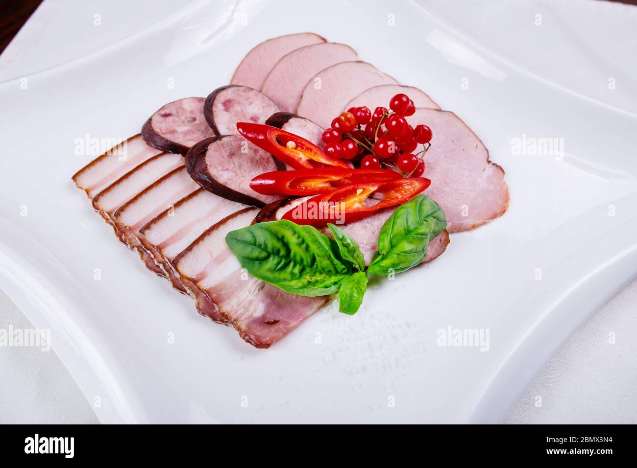 Bacon, ham and sausage on a white plate decorated greens and peppers Stock Photo