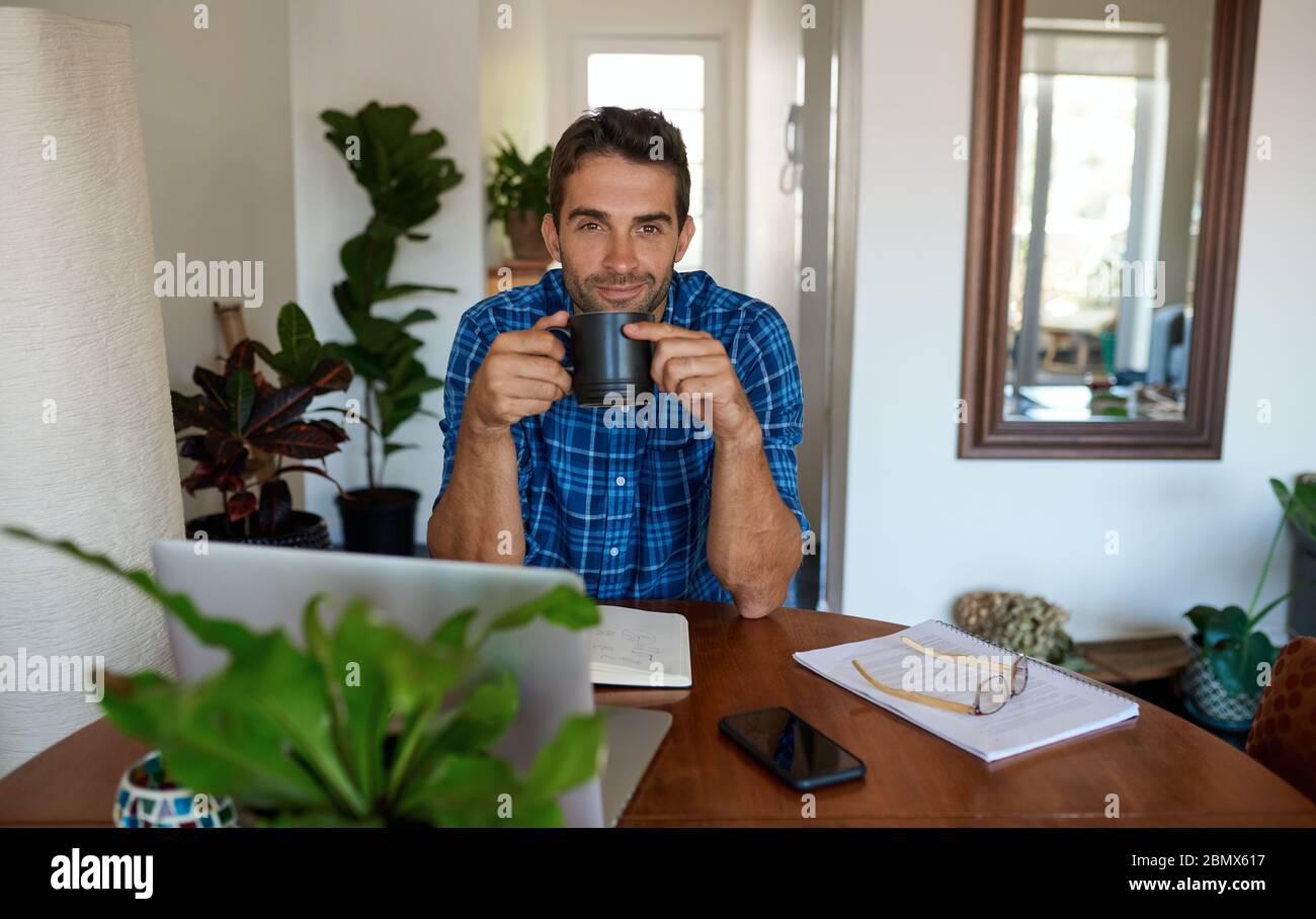 Smiling young man drinking coffee while working from home Stock Photo