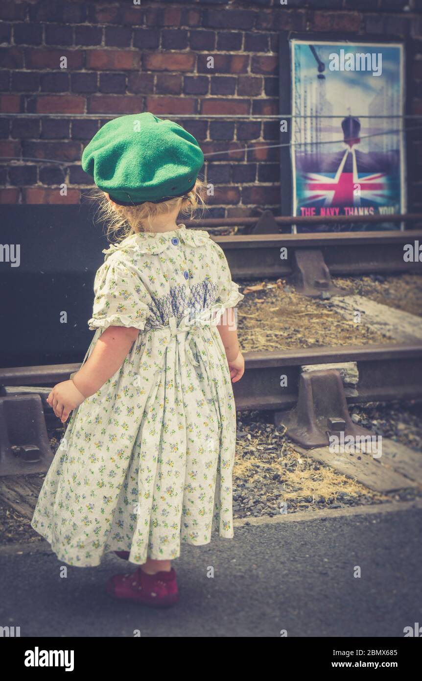 Rear view of cute little girl dressed in 1940s fashion as child of wartime WW2 Britain, 1940s heritage railway event UK. 1940s girl at vintage station. Stock Photo
