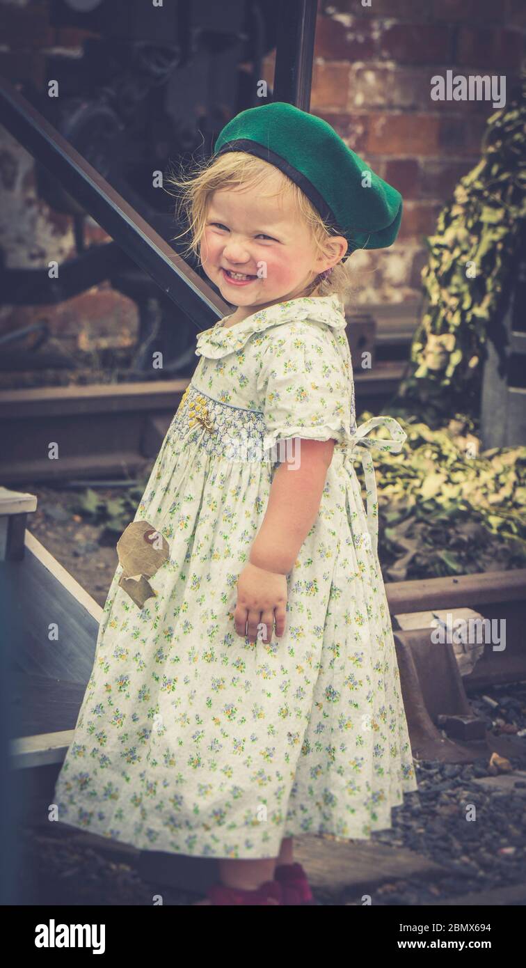 Retro view of isolated little girl smiling in 1940s dress as 1940 child of wartime WW2 Britain, 1940s heritage railway UK summer event. Stock Photo