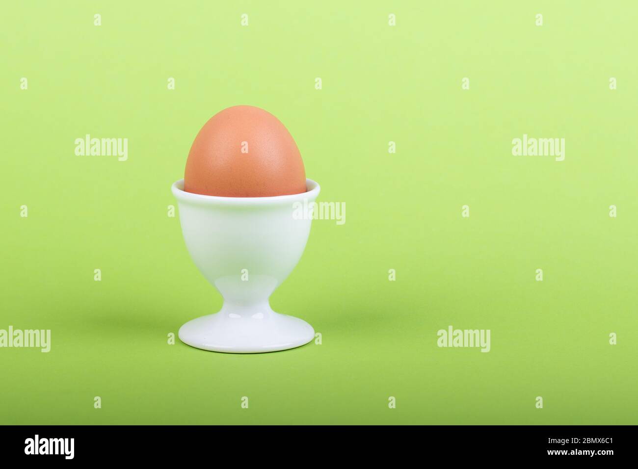 one brown egg in white egg cup before green background, close-up Stock Photo