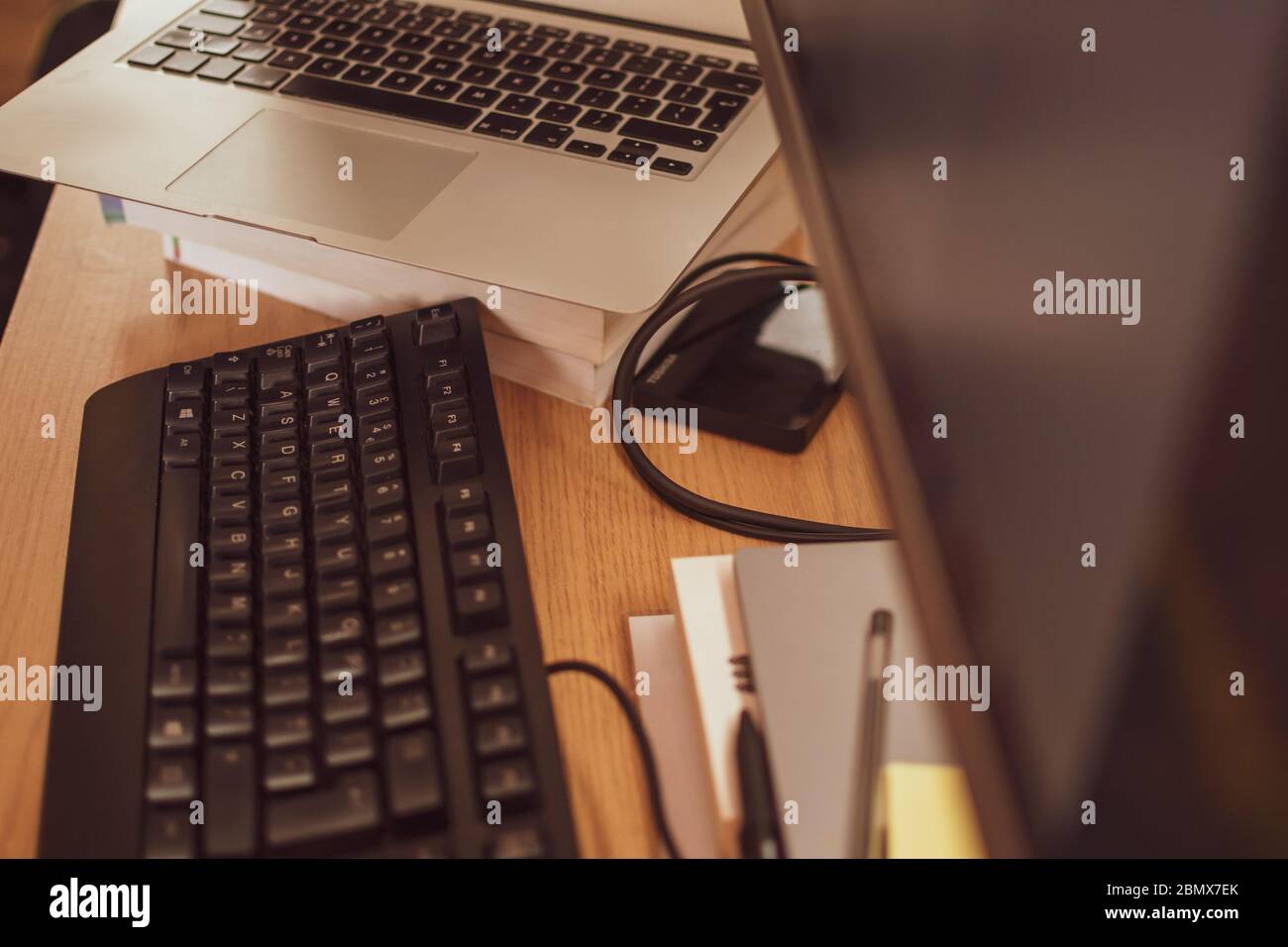 A busy modern home office set-up with a keyboard, laptop and monitor. Stock Photo