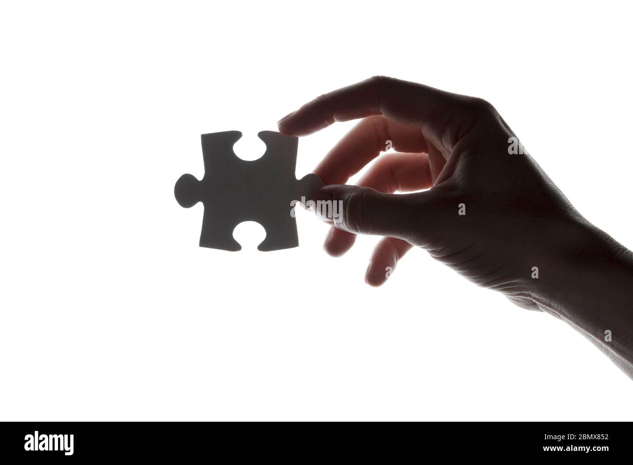 Silhouette of a hand holding a jigsaw puzzle piece on a white ...