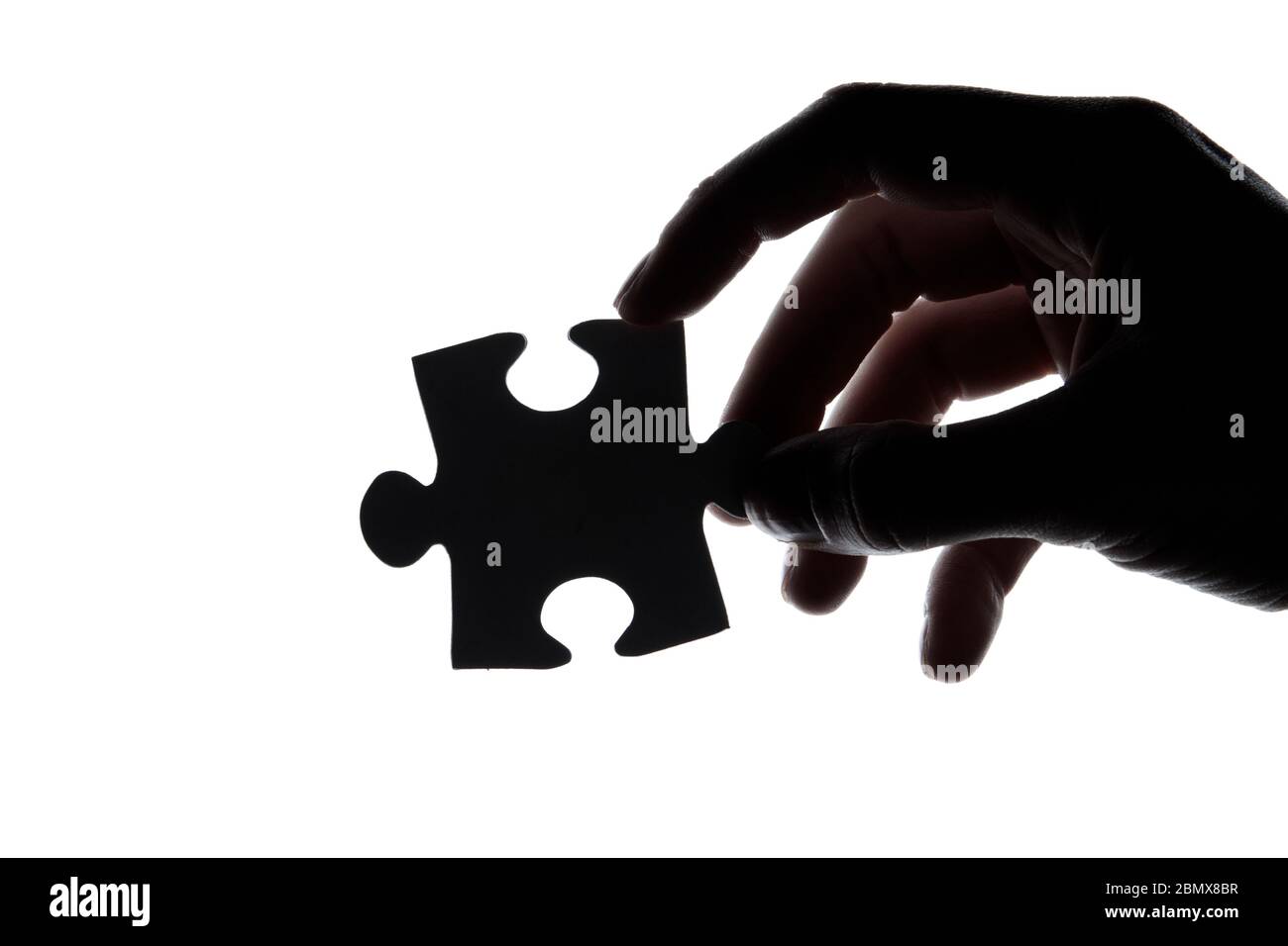 Silhouette of a hand holding a jigsaw puzzle piece on a white ...