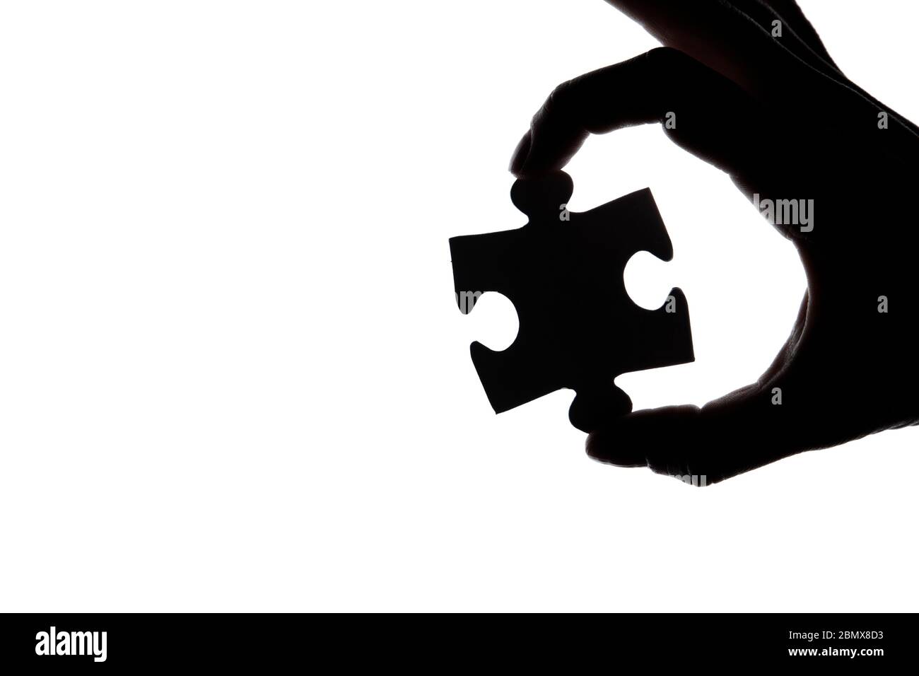 Silhouette of a hand holding a jigsaw puzzle piece on a white ...