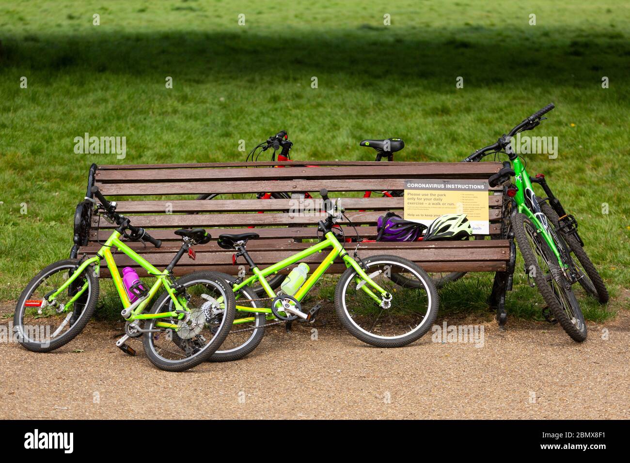 Bicycles leaning against a park bench bearing a coronavirus instruction sign in Clapham Common, during the covid-19 lockdown in London, 10 May 2020 Stock Photo