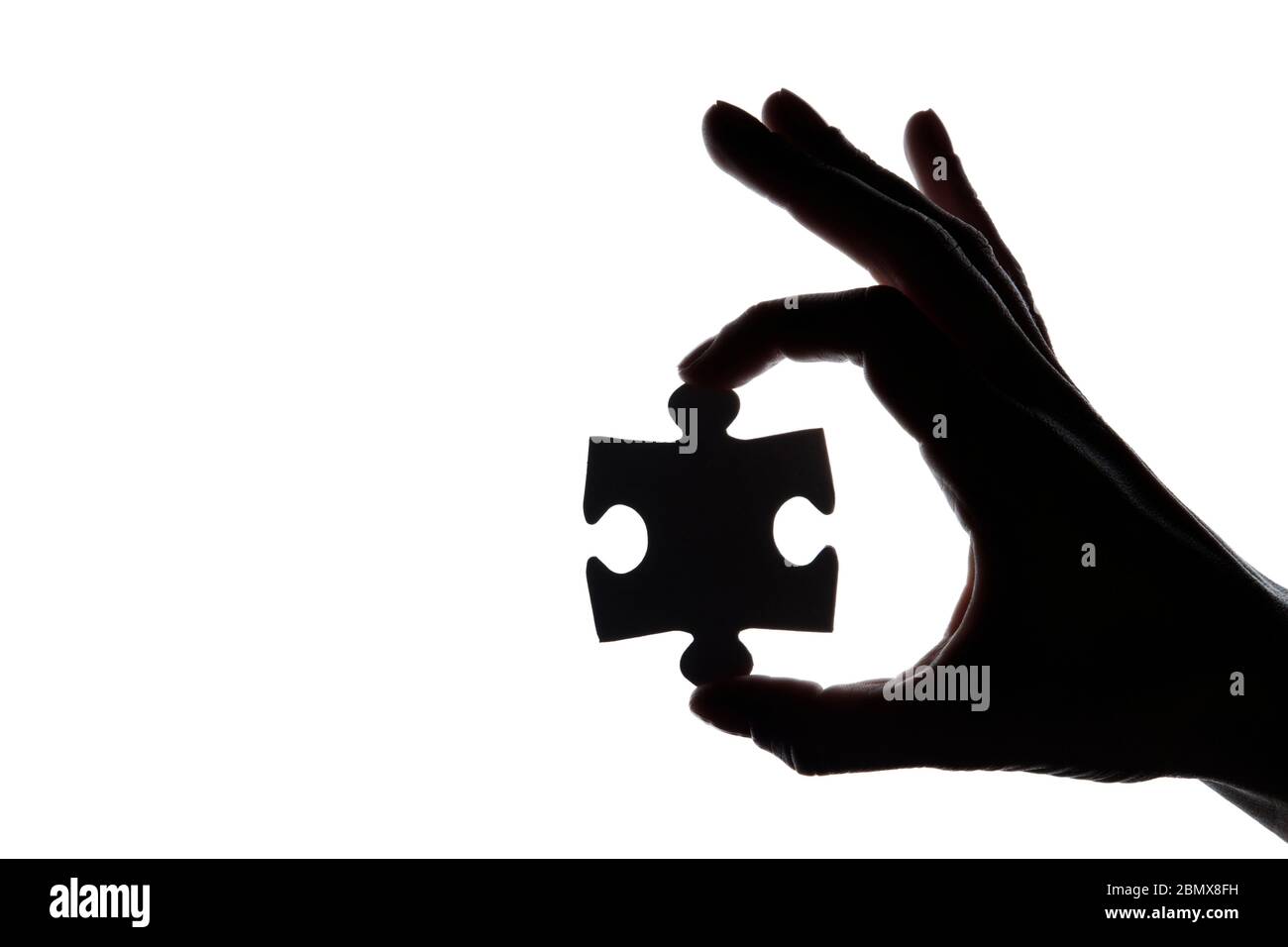 Silhouette of a hand holding a jigsaw puzzle piece on a white ...