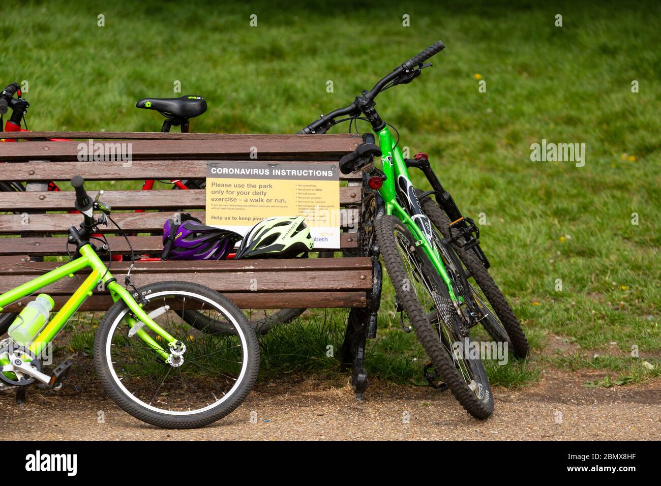 Bicycles leaning against a park bench bearing a coronavirus instruction sign in Clapham Common, during the covid-19 lockdown in London, 10 May 2020 Stock Photo