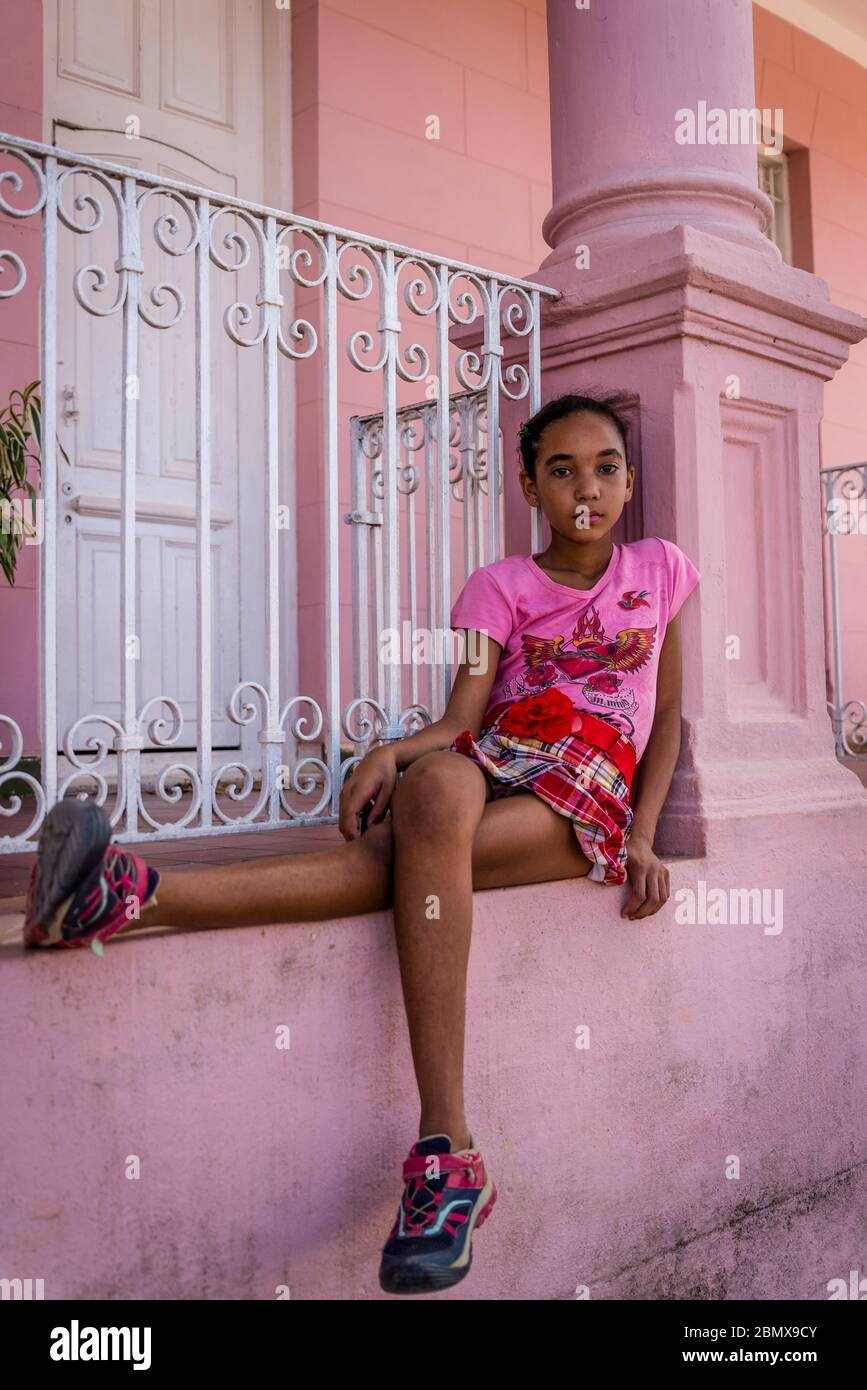 Ten year old girl sitting on a wall of a pink house, Vinales, Cuba Stock Photo