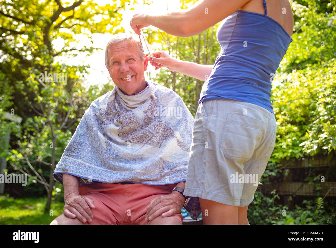 isolating Daughter in-law gives a haircut to her father in-law during lockdown in the garden during the coronavirus pandemic. Stock Photo