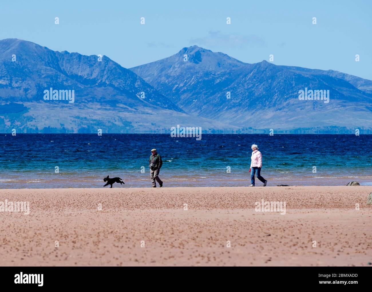 Seamill, North Ayrshire, Scotland, UK. 11th May, 2020. A couple walk their dog on the beach at Seamill in North Ayrshire with the Isle of Arran in the background. Credit: Chris McNulty/Alamy Live News Stock Photo