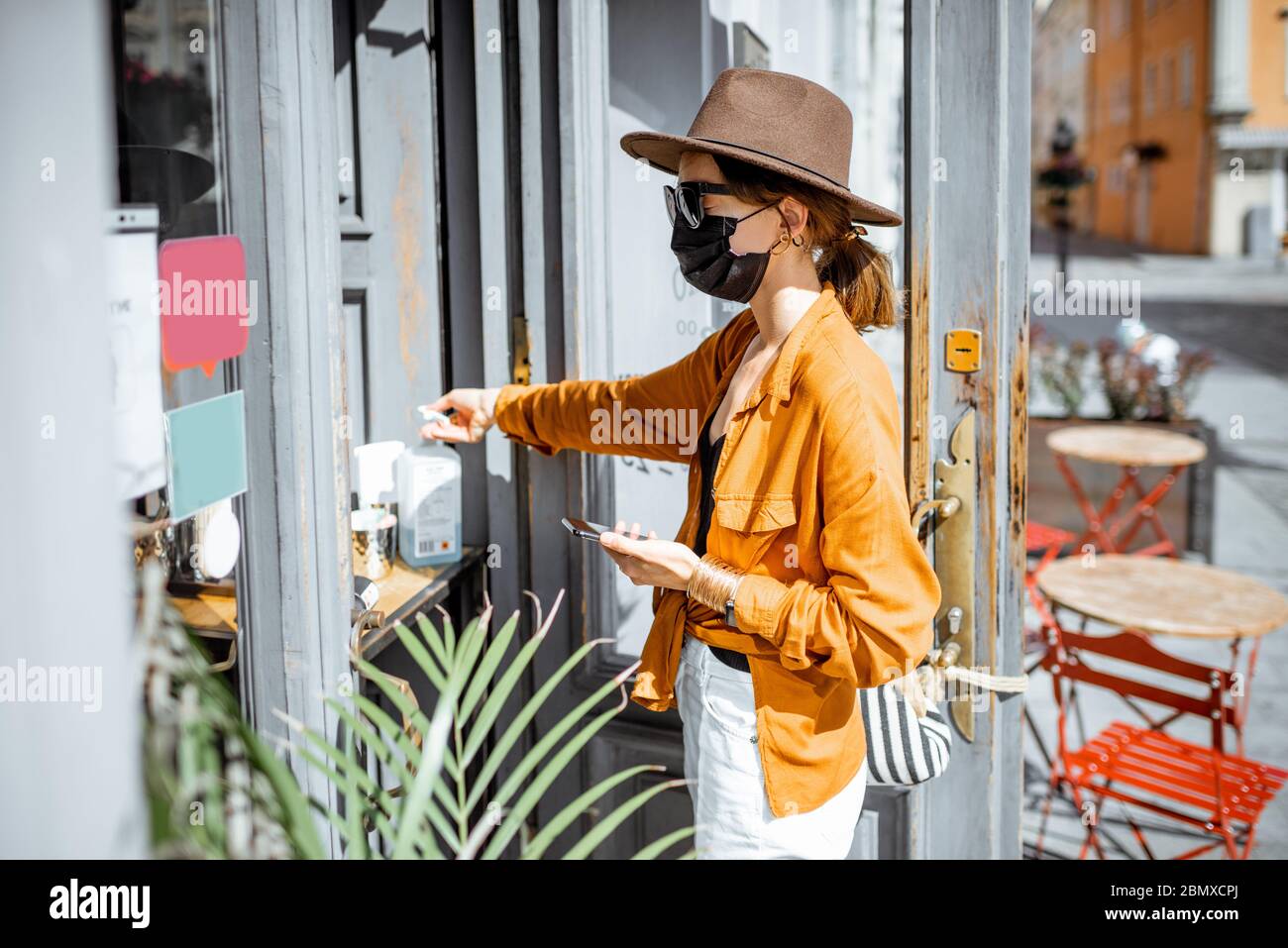 Woman in facial mask disinfecting her hands while making order for a take away food at the cafe outdoors. Concept of a new social rules after coronavirus pandemic Stock Photo