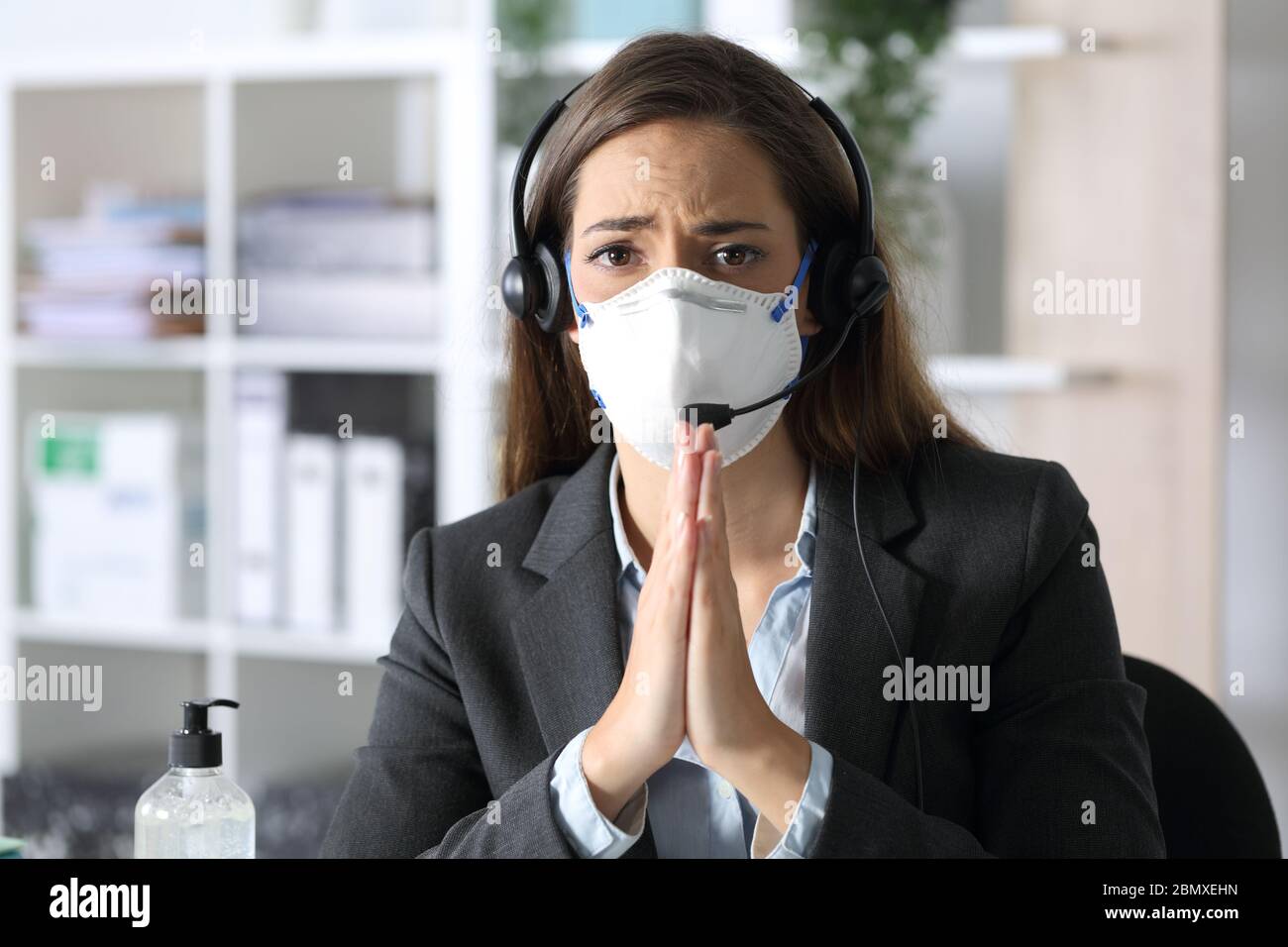 Sad telemarketer woman begging looking camera avoiding covid-19 with mask sitting at the office at night Stock Photo