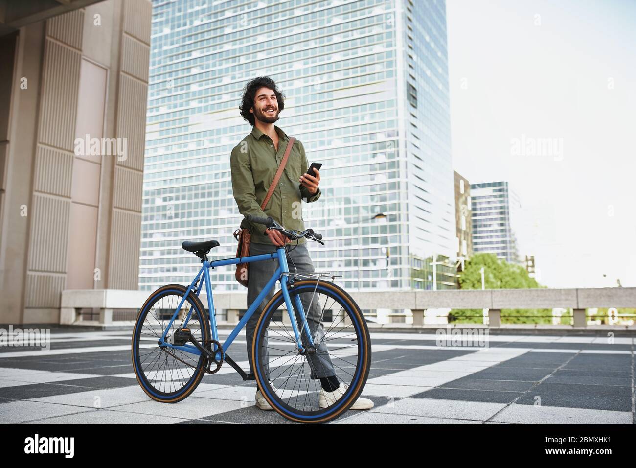 young man with blue cycle standing using smartphone while looking away Stock Photo