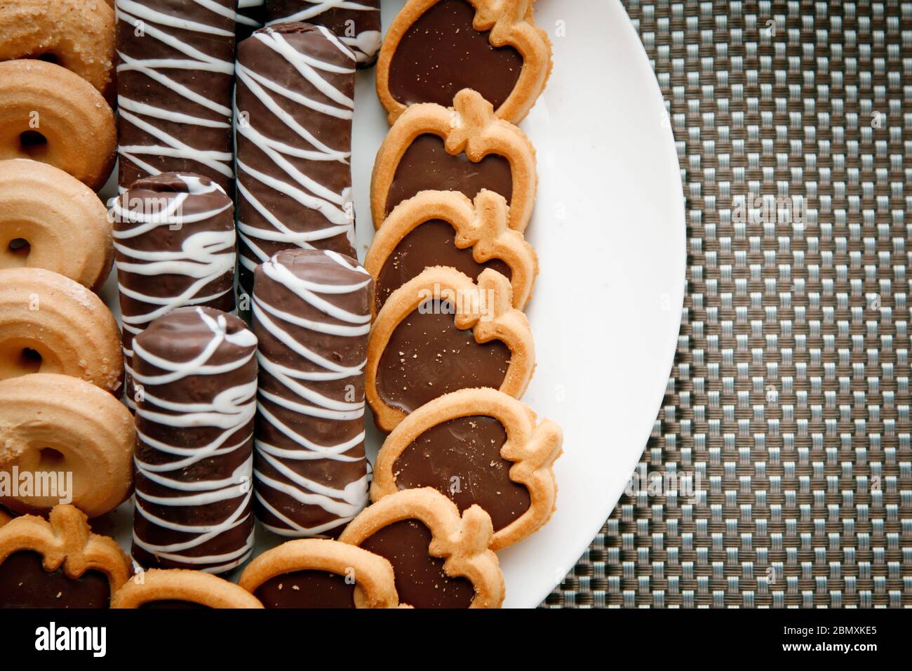 Chocolate oblong cookies, cookies in the form of ringlets and cookies in the form of apples lying on a white plate against the background of a gray wi Stock Photo