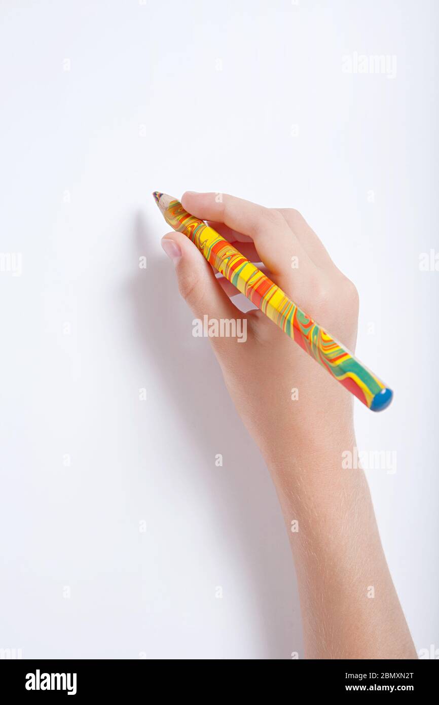 The child's hand holding a multicolored pencil against a white sheet of paper Stock Photo