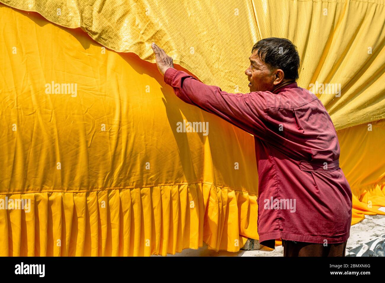 Old thai man stretches a yellow gaudy robe of a giant laying Buddha statue in Ayutthaya, Thailand, Asia Stock Photo