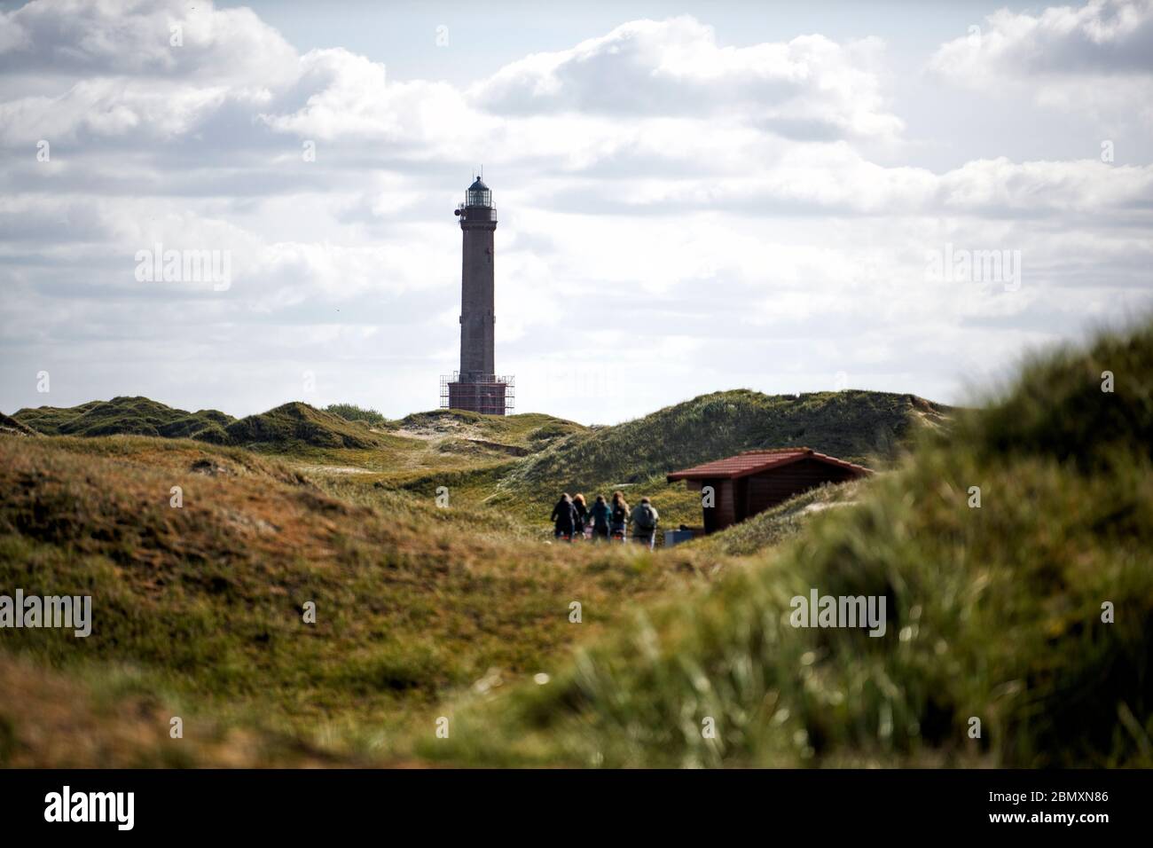 Der Leuchtturm von Norderney durch Duenen hindurch fotografiert mit einer Gruppe Wanderer auf dem Weg zu ihm. Stock Photo