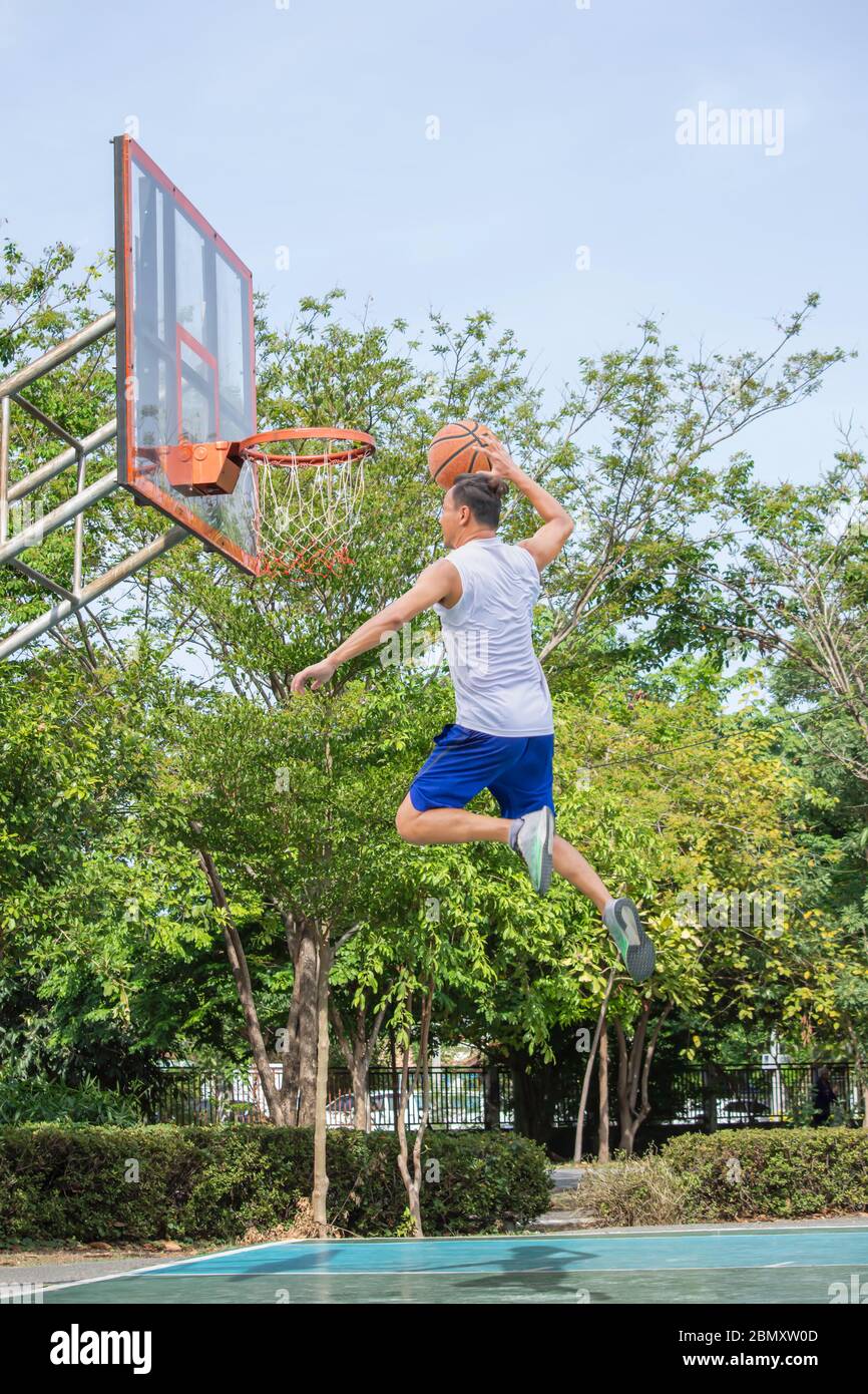 Basketball in hand man jumping Throw a basketball hoop Background tree in park Stock Photo Alamy