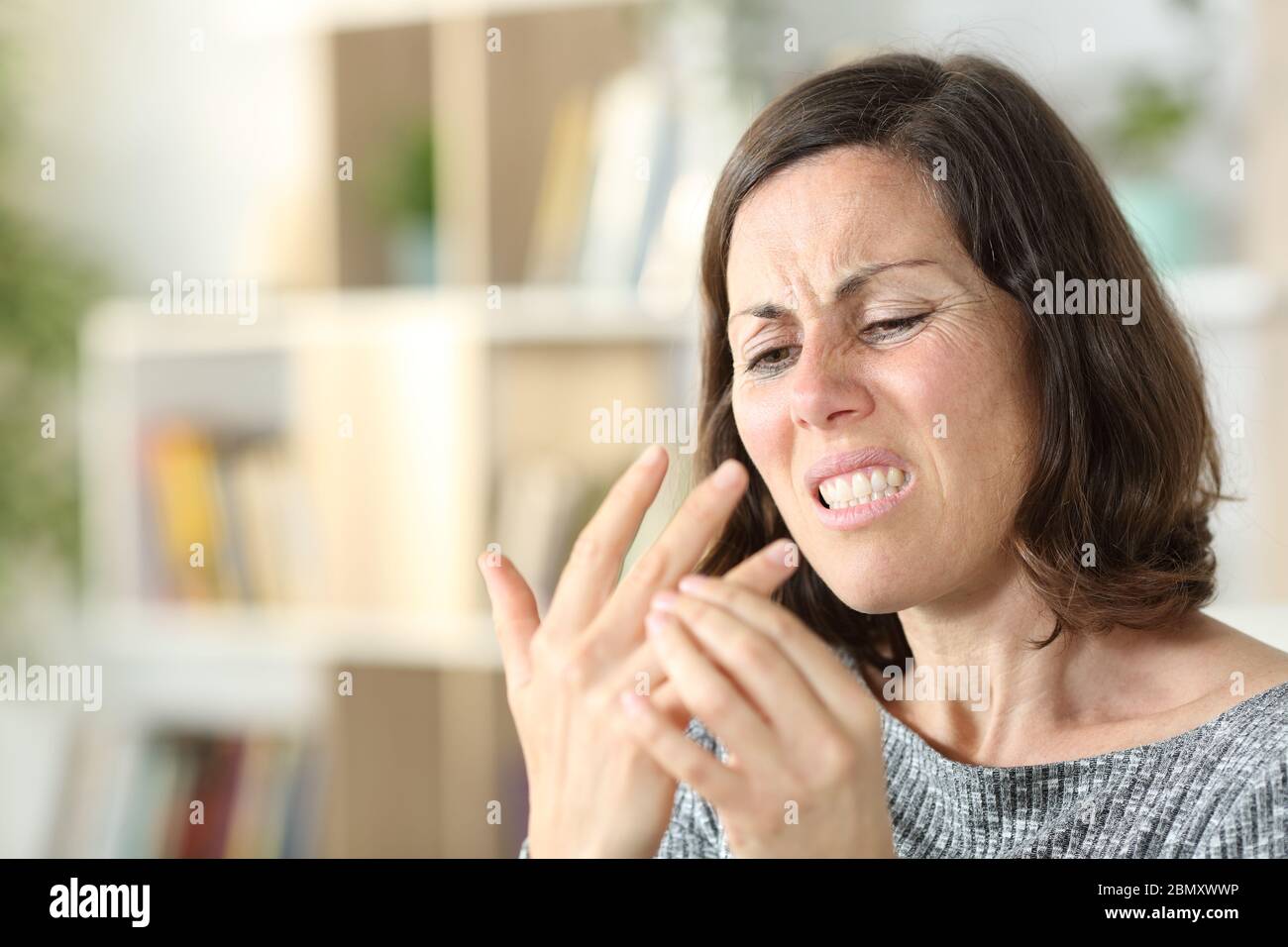 Adult woman with arthritis in pain touches joint in hand sitting in the living room at home Stock Photo