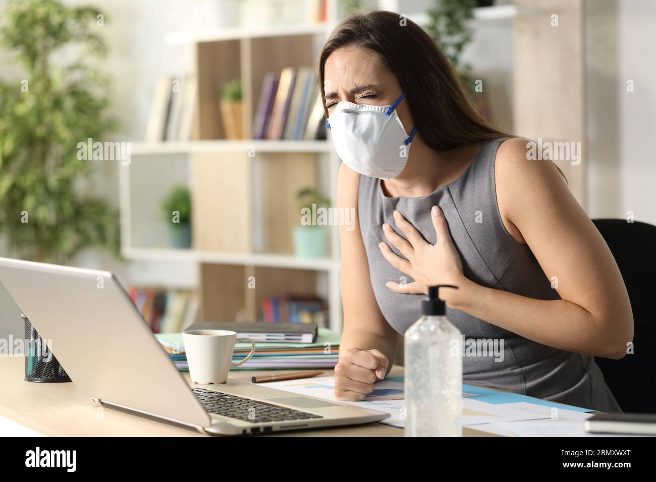 Entrepreneur woman with mask due covid-19 in pain wheezing sitting on a desk at homeoffice Stock Photo