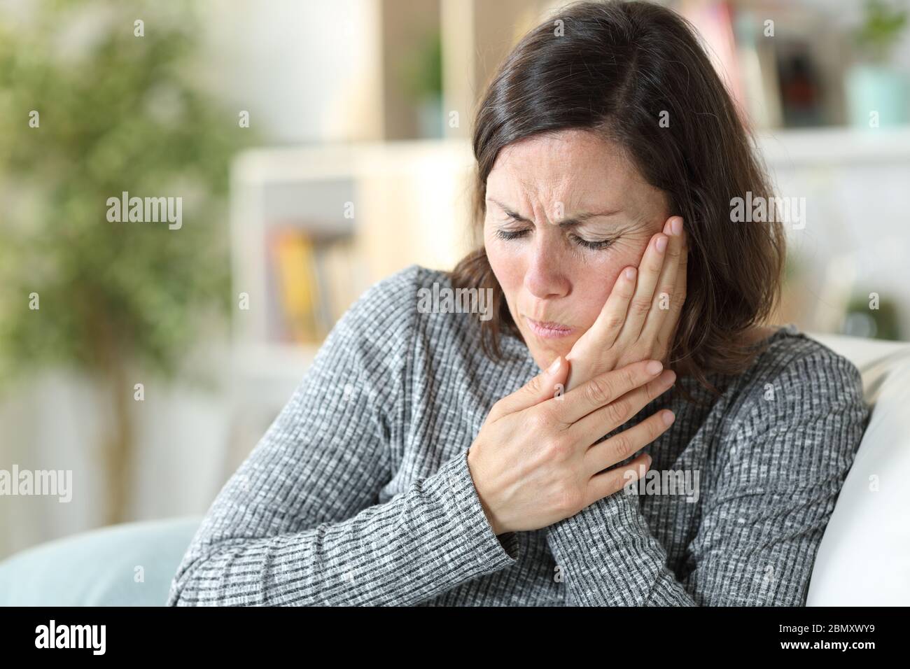 Middle age woman in pain suffering toothache touching face sitting on a couch at home Stock Photo