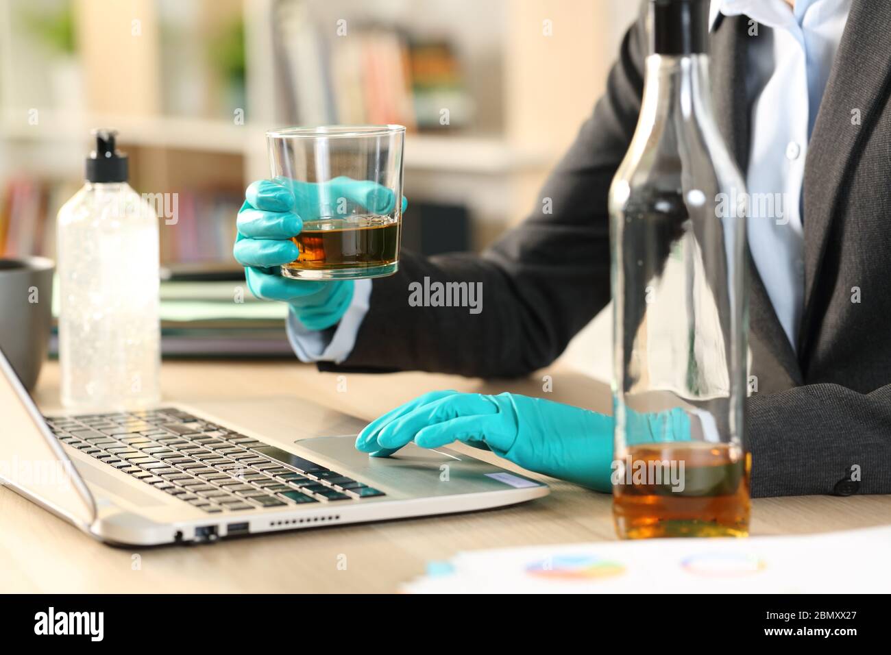 Close up of entrepreneur woman hands drinking alcohol working on laptop on coronavirus confinement sitting on a desk at home office Stock Photo