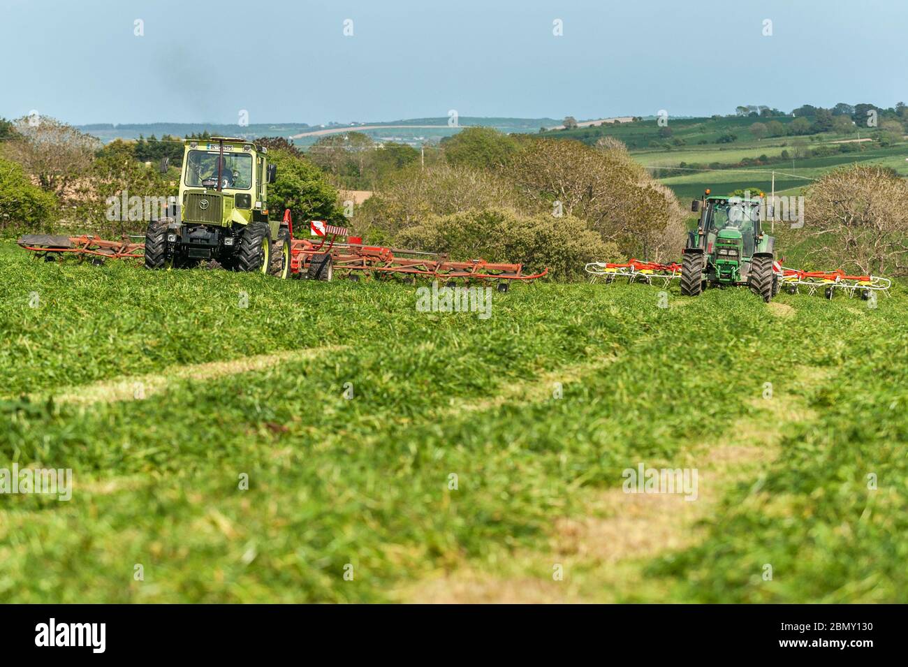 Timoleague, West Cork, Ireland. 11th May, 2020. An MB Trak 900, driven by David Deasy, and John Deere 6620, driven by Kevin Cahalane, towing an SIP 1100 Tedder and Pottinger 900 respectively, aerate grass for silage on the farm of David Deasy of Timoleague. The grass will be bailed tomorrow. Credit: AG News/Alamy Live News Stock Photo