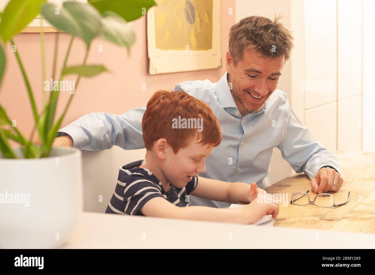 Dad helping pre-teen boy with his school work at home during homeschooling due to the coronavirus lockdown. Landscape format. Stock Photo