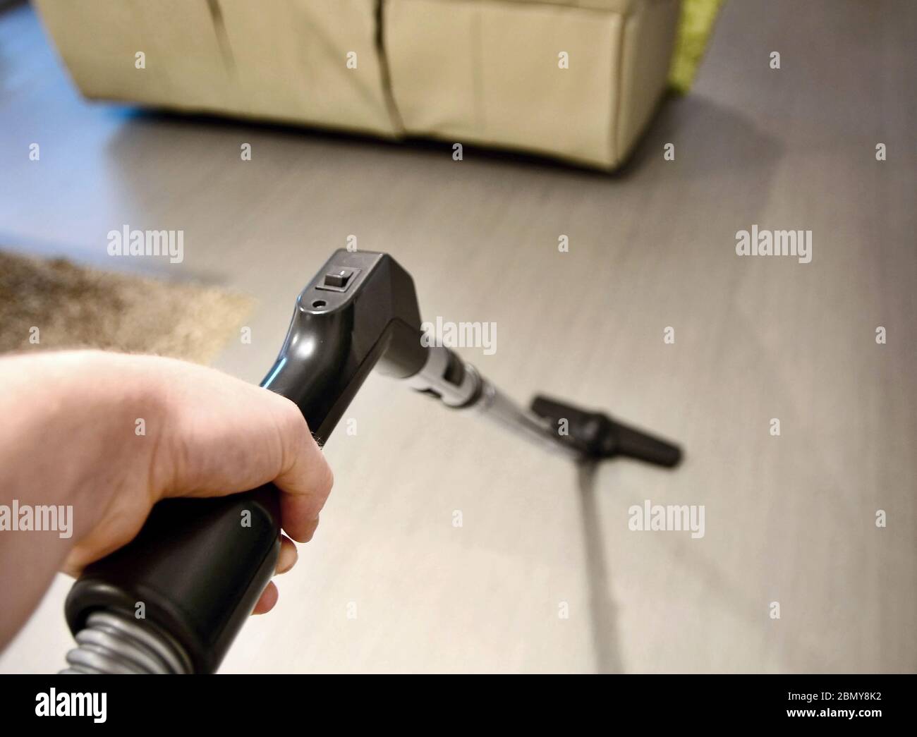 Man hand holding vacuum cleaner tube and makes housework and vacuuming the floor in room. Closeup point of view or first person view shot. Stock Photo
