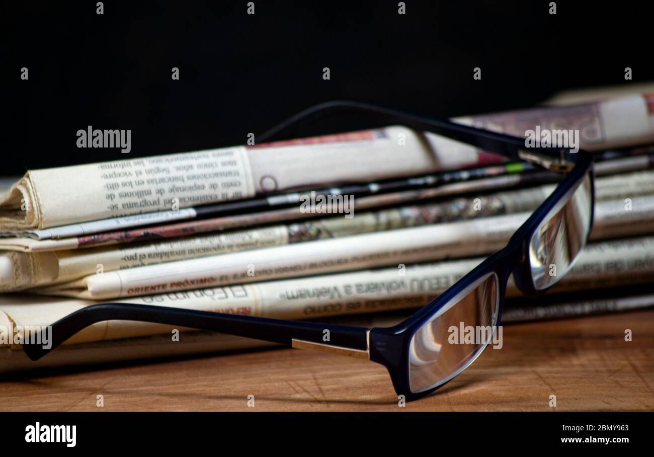 folded pile newspapers with a pair of blue reading glasses on it. free information and press concept Stock Photo
