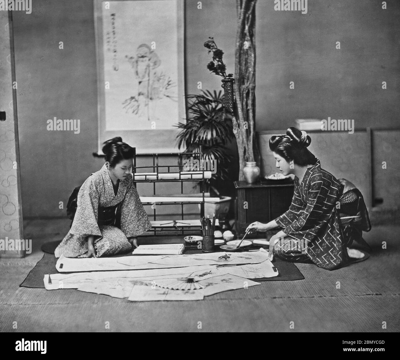 [ 1890s Japan - Japanese Calligraphy ] —   Woman in kimono painting on a kakemono (掛物), a hanging scroll .  Kakemono are used to display and exhibit paintings and calligraphy. They are usually mounted on a flexible backing with silk fabric edges, so that they can be rolled for storage.  From a series of glass slides published (but not photographed) by Scottish photographer George Washington Wilson (1823–1893). Wilson’s firm was one of the largest publishers of photographic prints in the world.  19th century vintage glass slide. Stock Photo