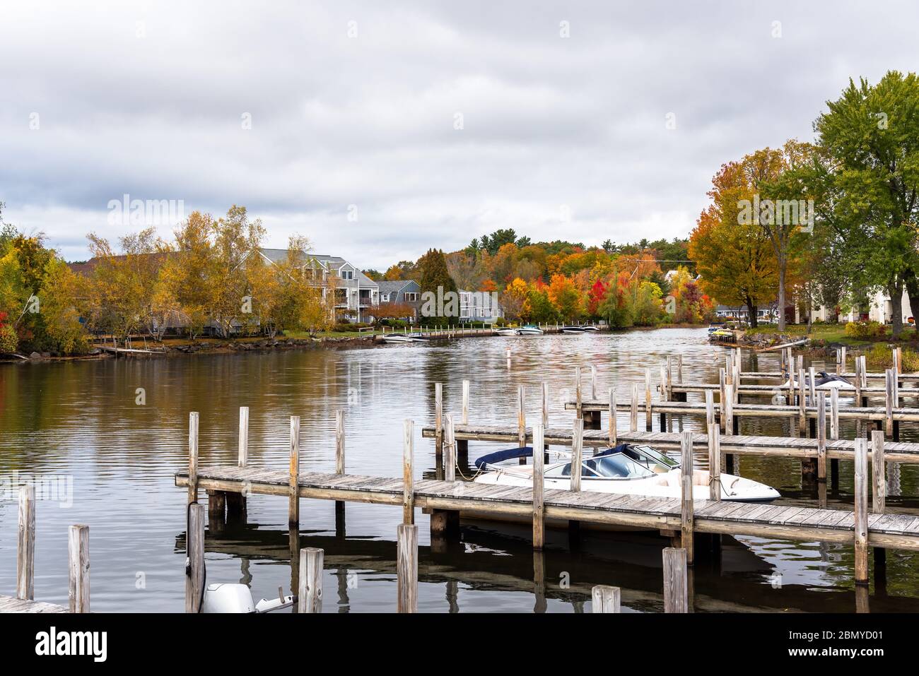 Wooden jetties on a river on a cloudy autumn day. Riverside apartment buildings and colouful autumnal trees are on the other side of the river. Stock Photo