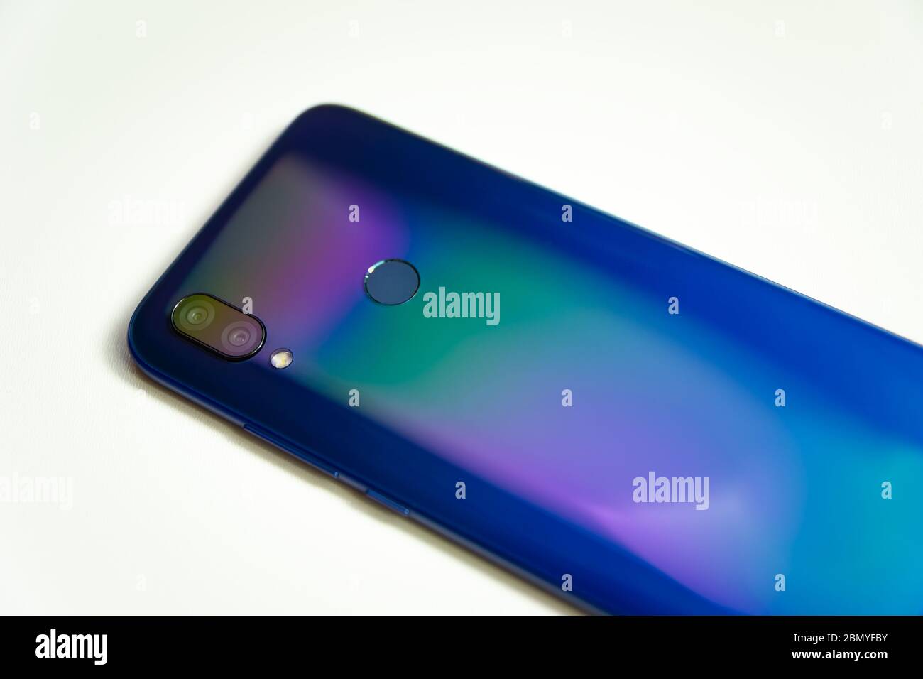 The back of a blue smartphone with two cameras and a flash, illuminated with colored light on a white background Stock Photo