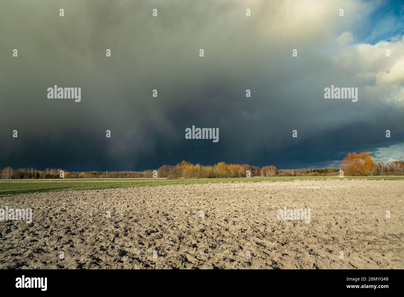Huge dark hail cloud over the plowed field, view on a spring sunny day Stock Photo