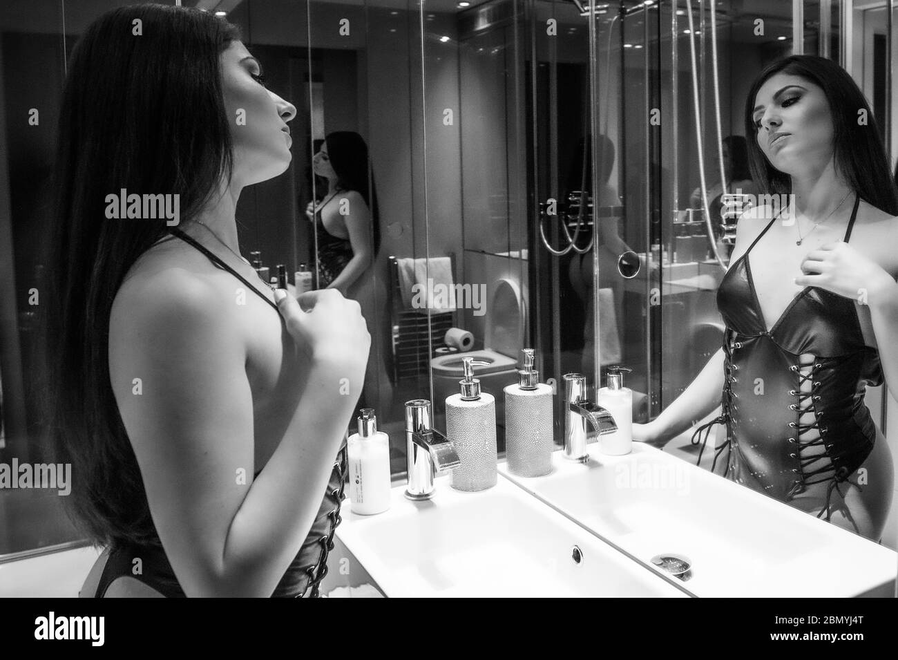 A black and white image of a young caucasian woman looking at a mirror wearing lingerie at a boudoir location. Stock Photo
