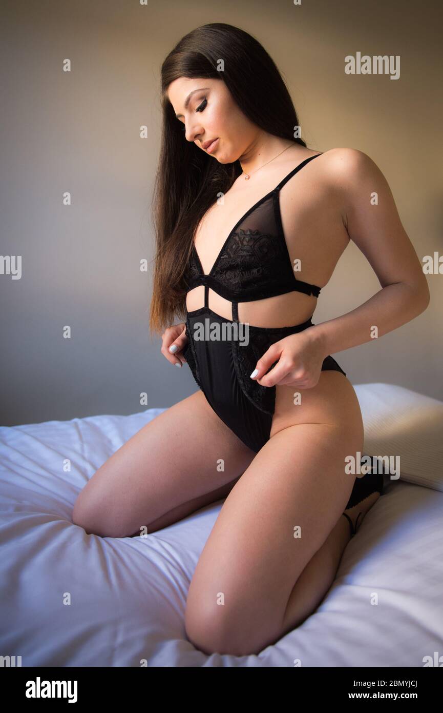 A young caucasian woman kneels on a bed wearing lingerie at a boudoir location. Stock Photo