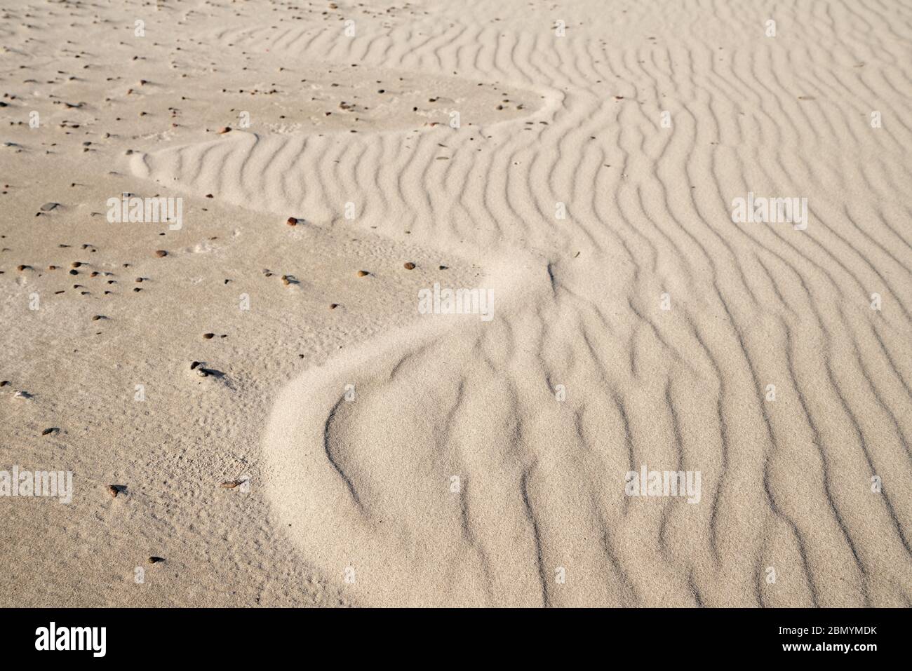 Small sand waves create a pattern, the wavy area ends in an arch and merges into an area covered with small stones Stock Photo