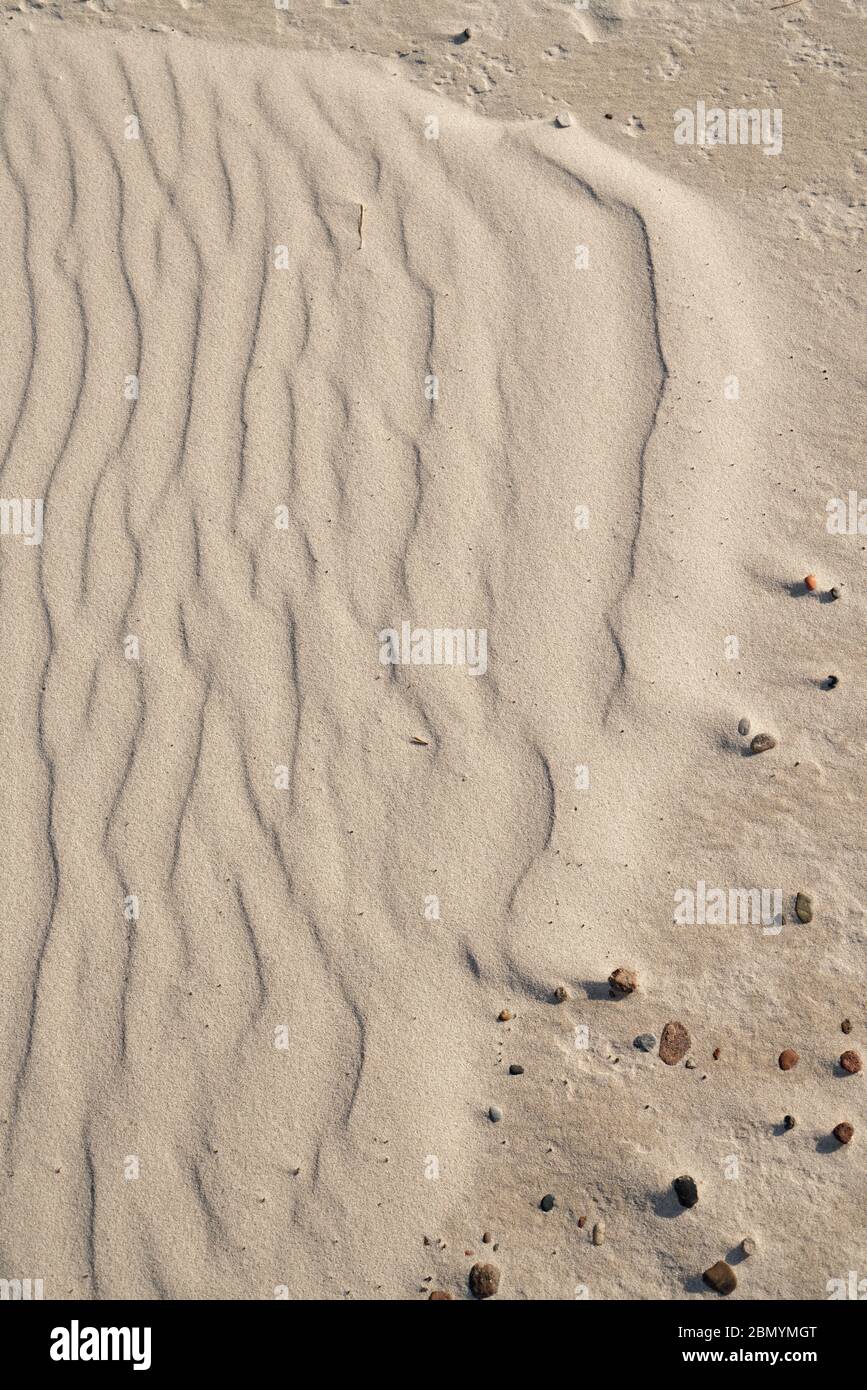 Small sand waves create a pattern, the wavy area ends in an arch and merges into an area covered with small stones Stock Photo