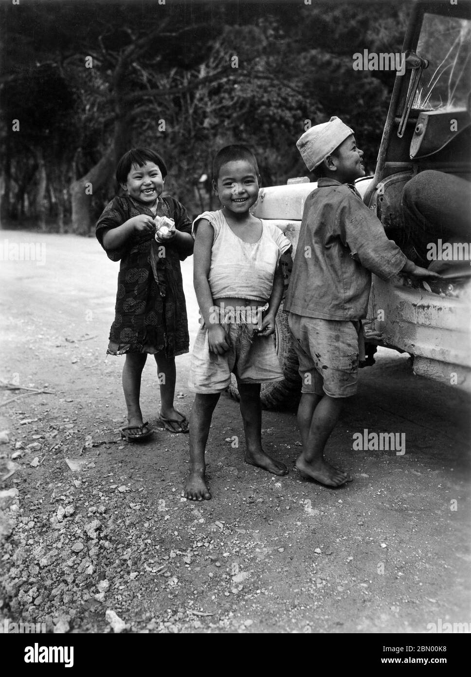 [ 1946 Japan - Okinawan Children ] —   Okinawan children begging for candy next to a US military Jeep, 1946 (Showa 21).  20th century gelatin silver print. Stock Photo