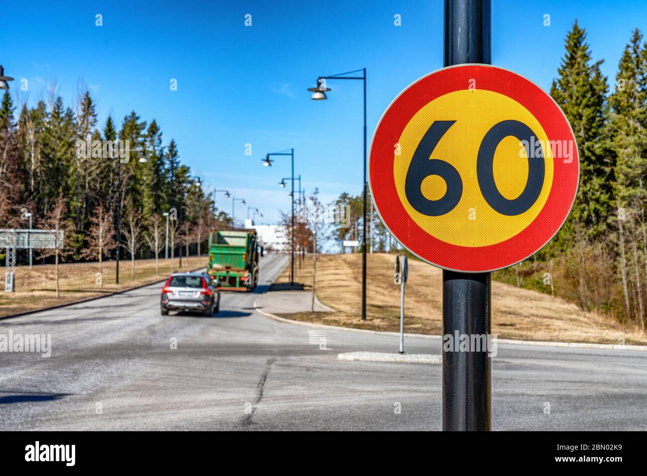 Beautiful close up photo of fresh 60 km speed limit traffic sign mounted on black pole. Blurry background with one car and truck driving on leading to Stock Photo