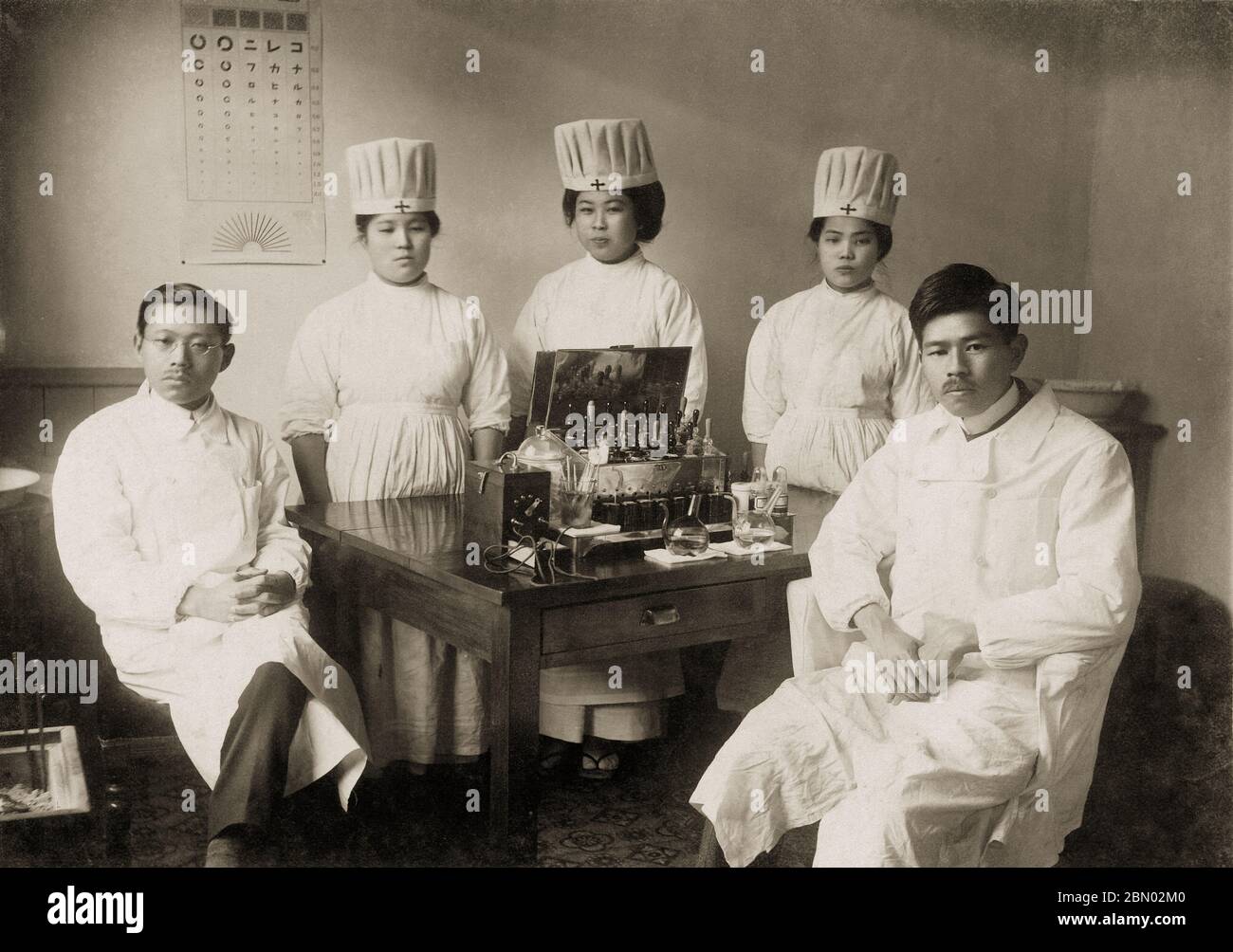 [ 1910s Japan - Japanese Doctors and Nurses ] —   Doctors and nurses posing in uniform, ca. 1910s. A Japanese eye chart hangs on the wall.  20th century gelatin silver print. Stock Photo