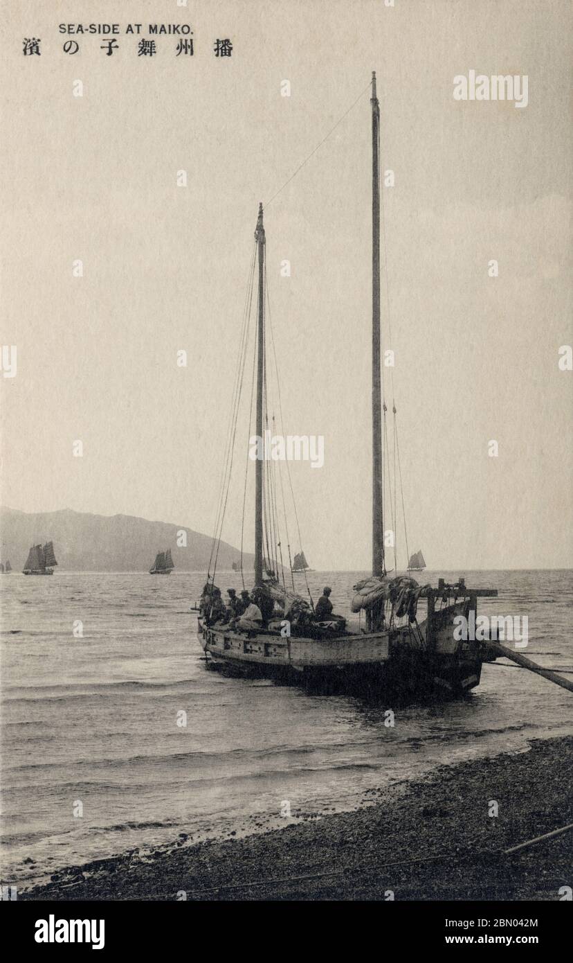 [ 1920s Japan - Japanese Sailing Vessels ] —   A sailing vessel with fishermen at Maikonohama (舞子の浜) in Suma (須磨) near Kobe, Hyogo Prefecture.  On the horizon, Awajishima (淡路島) can be seen.  Suma-mura (須磨村) became Suma-machi (須磨町) in 1912 (Meiji 45), and part of Kobe City in 1920 (Taisho 9). In 1931(Showa 6), it became a full-fledged ward of Kobe and the area is now called Suma-ku (須磨区).  20th century vintage postcard. Stock Photo