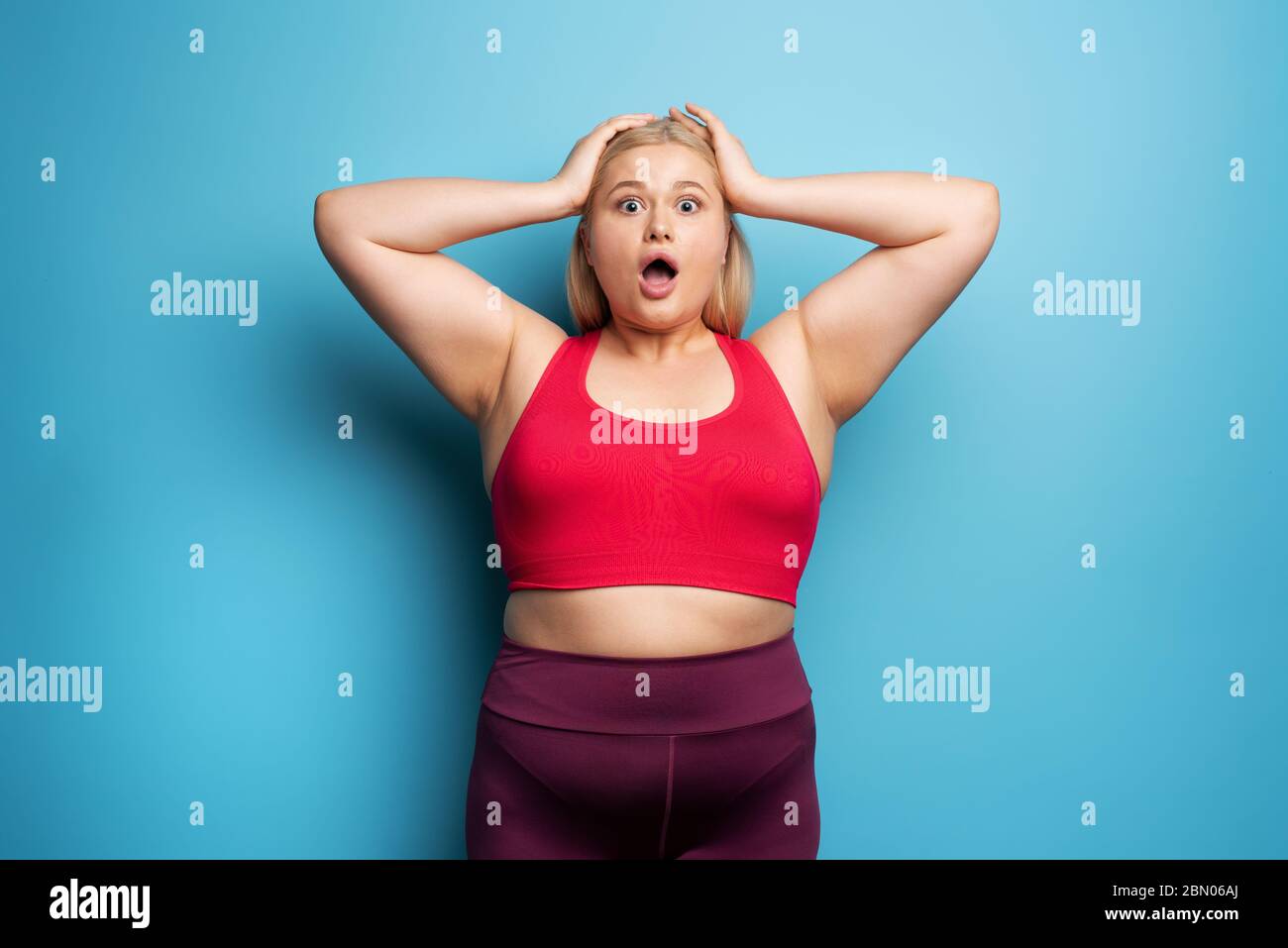 Fat girl is worried because the scale marks a high weight. Cyan background Stock Photo