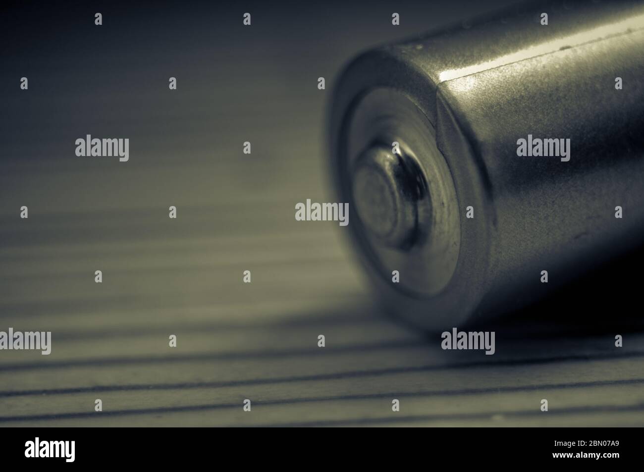 Closeup of the positive end of an AA battery on a wooden surface in tinted monochrome showing concepts of power and sustainability Stock Photo