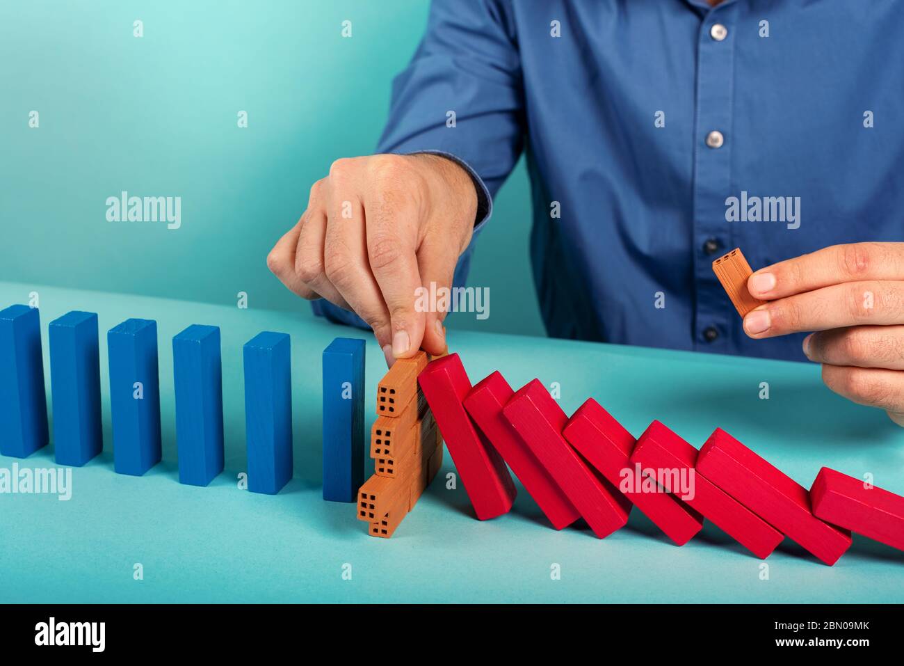 Businessman stops a chain fall like domino game. Concept of preventing crisis and failure in business. Stock Photo