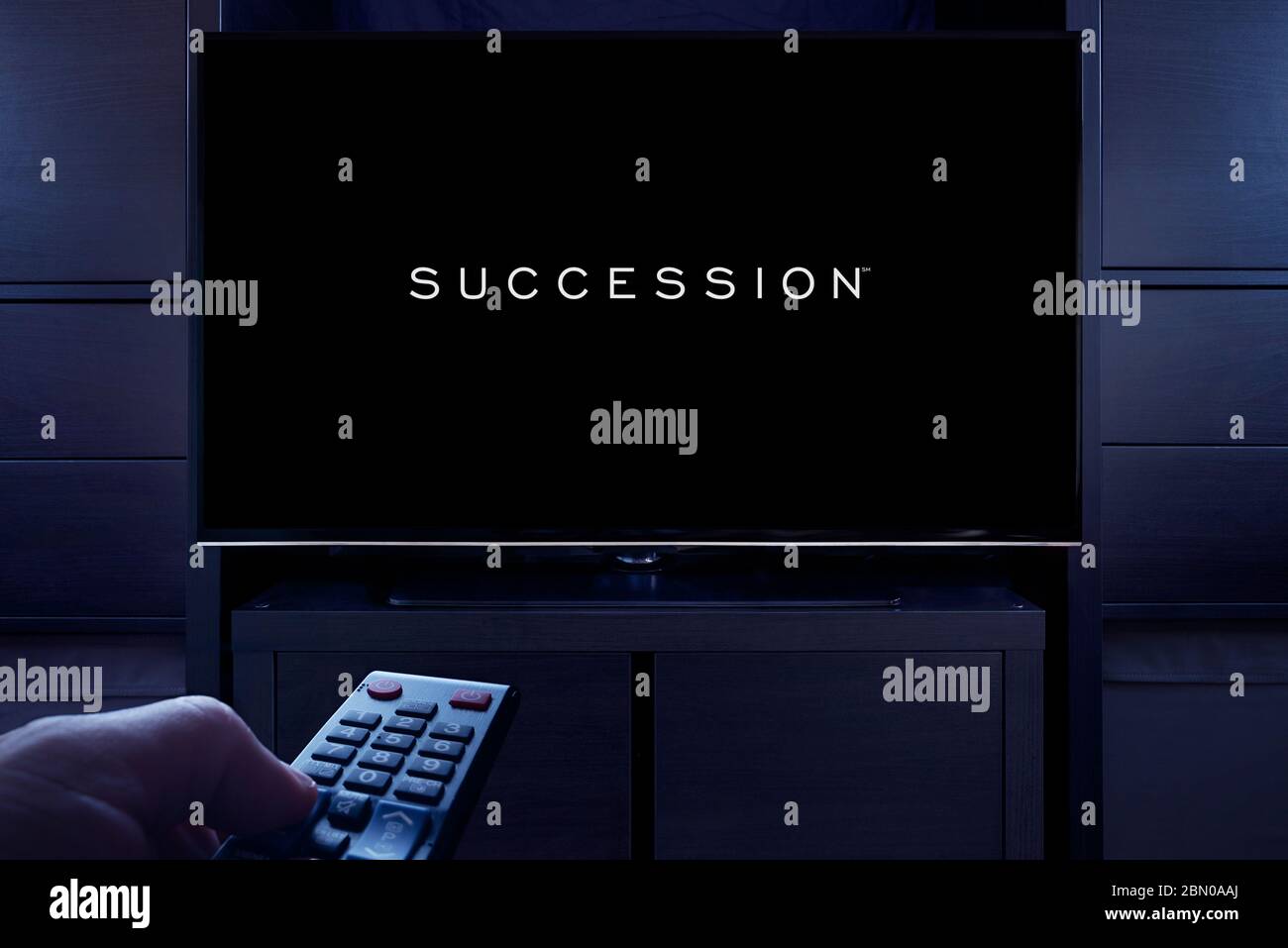 A man points a TV remote at the television which displays the Succession main title screen (Editorial use only). Stock Photo