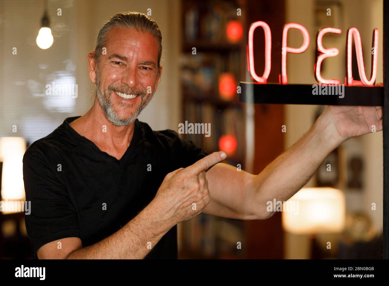 open for business concept, small business owner reopening premises after covid-19 virus pandemic, happy man pointing to red neon open sign cafe bar Stock Photo