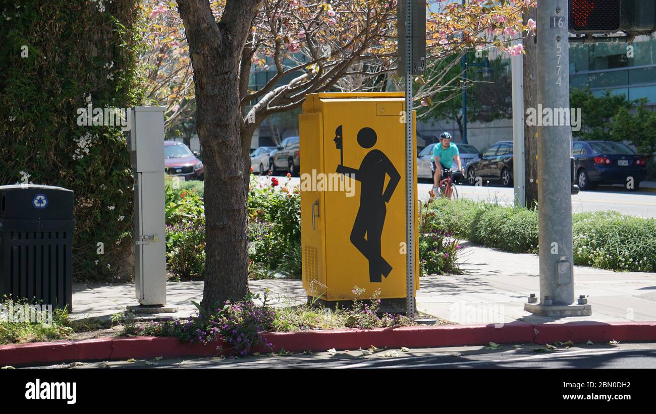 Pedestrian man holding a mask on a utility box, created by artist   Seyed Alavi with bicyclist passing by. Emeryivlle, California. Stock Photo